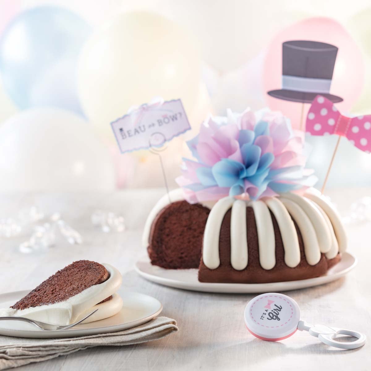 A gender reveal bundt cake with a decoration of a top hat and a pink dotted bow tie. A card reads Beau or Bow? and the center of the cake has a pink and blue bow. 