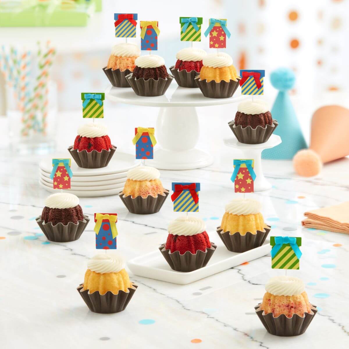 Cupcake-sized mini cakes with frosting and birthday present toppers with different celebratory designs.