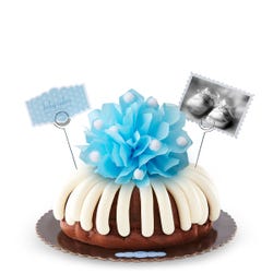 A bundt cake with a blue bow in the center with a small photo card of baby shoes and a blue dotted card that reads baby cakes. Sweet congratulations!. 
