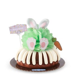 A bunny bundt cake with a mint colored bow in the center. Decorated with plush bunny rabbit ears, velvet feet and a cut carrot cutout. 