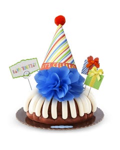 A bundt cake with frosting topped with a party hat that says Let's Celebrate. Two wrapped gift boxes are on the sides along with a card that reads Happy 'Bundt'day.