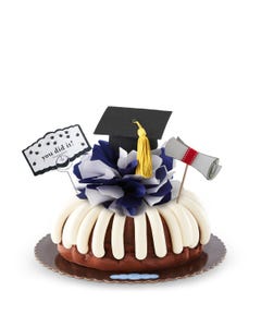 Bundt cake with frosting and topped with a customizable colored bow. It is topped with a diploma rolled up and a graduation cap with a tassel and a card that says you did it!.