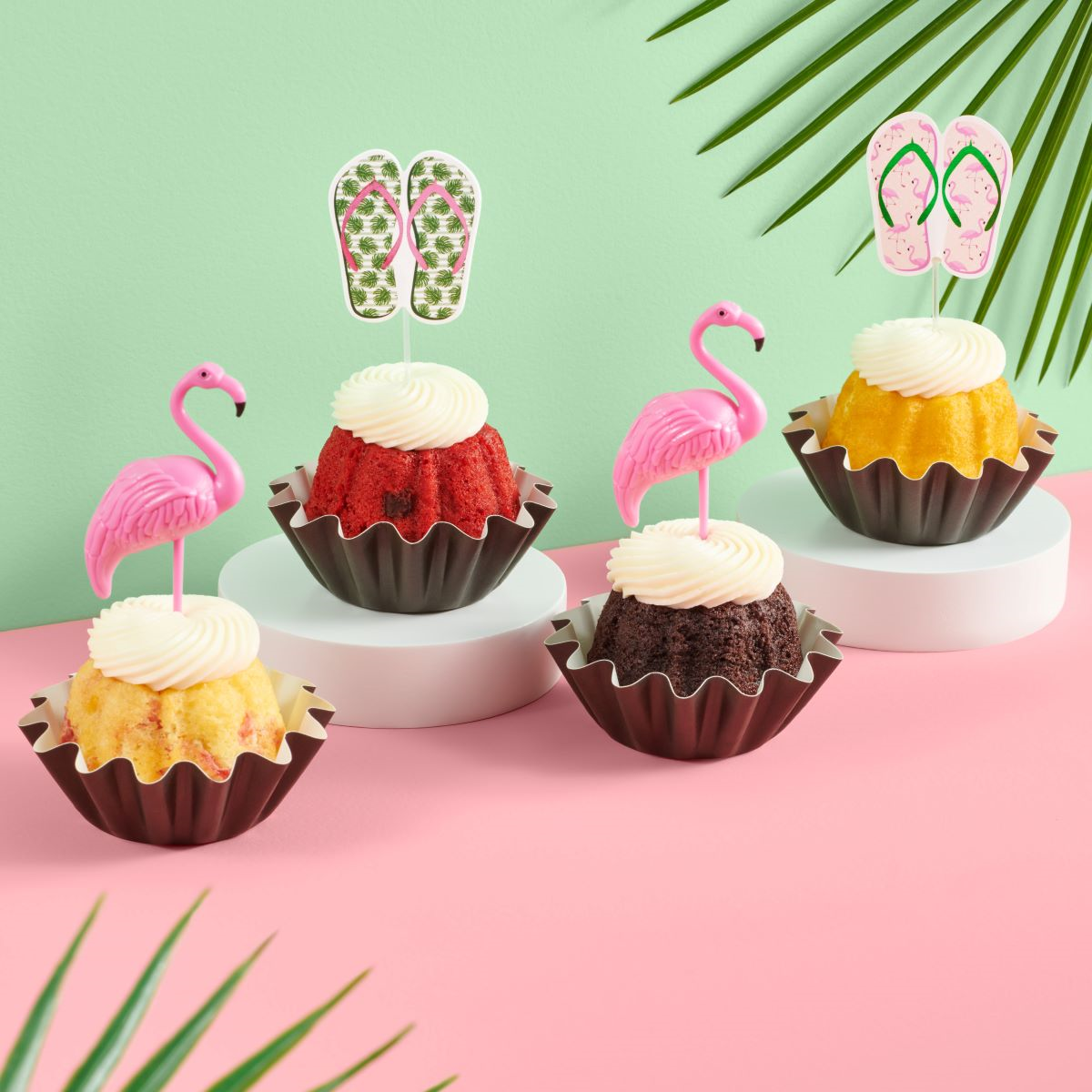 Mini bundt cakes decorated with a topper: from left to right, there's a pair of green tropical flip-flops, a pink flamingo, another pair of pink flip-flops with green straps, and another pink flamingo.