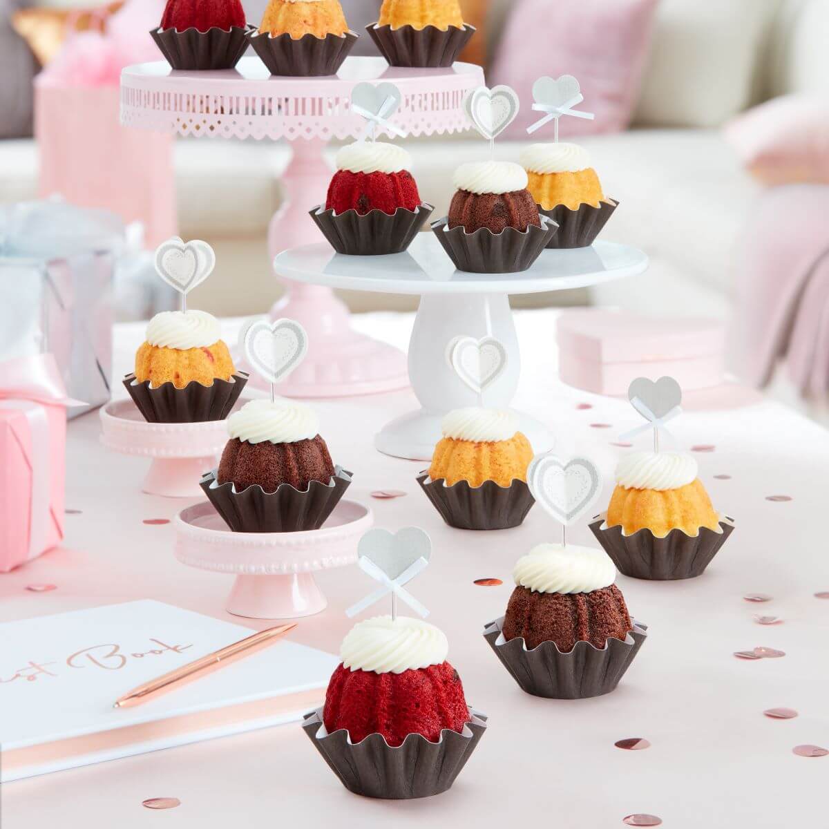 Four mini Bundt cakes each adorned with a delicate white heart topper, presented in a row showcasing a variety of cake flavors.