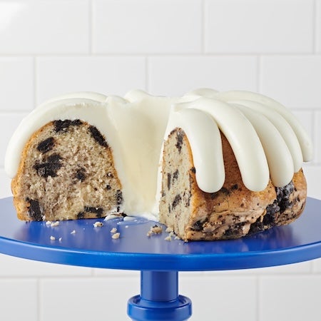 Oreo Cookies and Cream Bundt cake on a cake stand, a slice cut out showing the middle of the cake with Oreo pieces - Shop Bundt Cakes