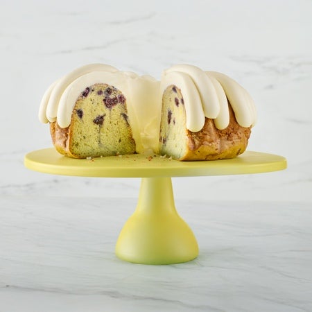 Lemon Blueberry Bundt cake on a cake stand, a slice cut out showing the middle of the cake with - Shop Bundt Cakes