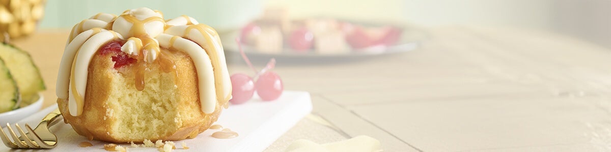 Pineapple Upside Down Bundtlet showing the middle of the cake topped with frosting, drizzle and cherry - Limited Time only