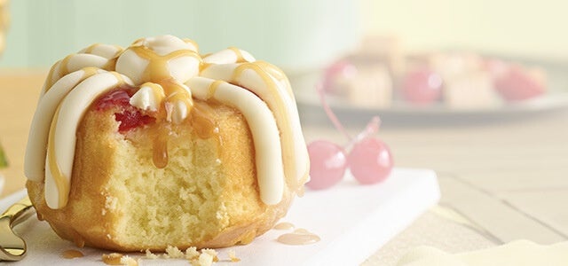 Pineapple Upside Down Bundtlet showing the middle of the cake topped with frosting, drizzle and cherry - Limited Time only